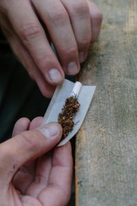 Detailed close-up photo of hands carefully rolling a tobacco joint on wood surface.