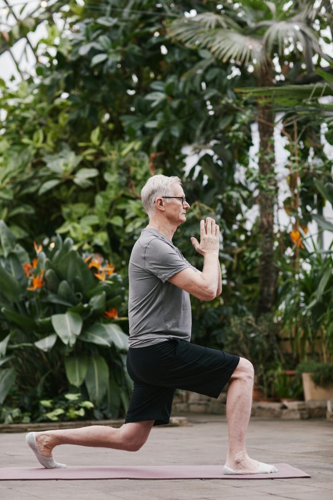 A senior man gracefully performs a yoga pose in a lush botanical garden, embodying mindfulness and well-being.